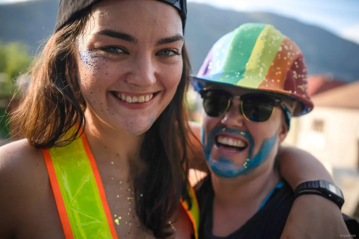 Two smiling volunteers in glitter, one wearing a rainbow hard hat and the other a hi-vis vest